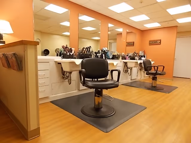 Salon area with two styling chairs and washing sinks beneath mirrors in a warm-toned room.