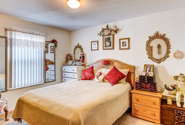 Cozy decorated bedroom with a bed topped by red accent pillows, wooden headboard, nightstands, dresser and wall mirrors.