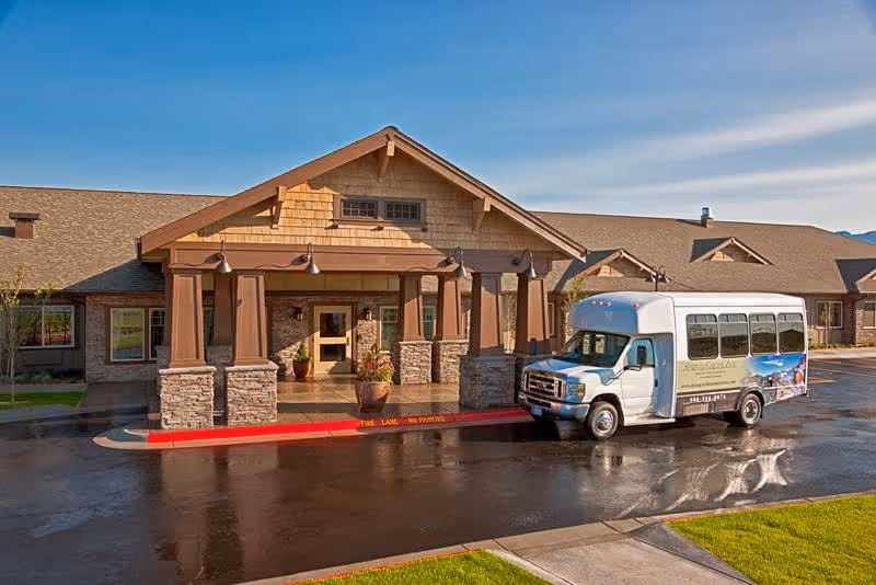 Front entrance of Canyon Creek Memory Care Community with a covered porte-cochère and a parked shuttle bus.