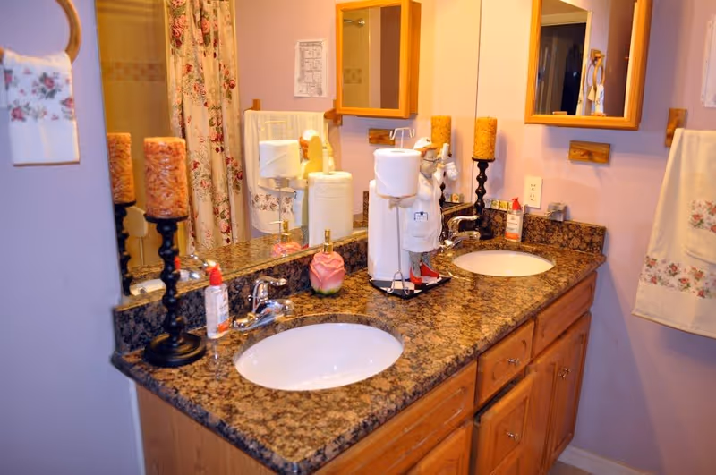 Double-sink bathroom vanity with a granite countertop, two mirrors, decorative candles, and bathroom accessories.