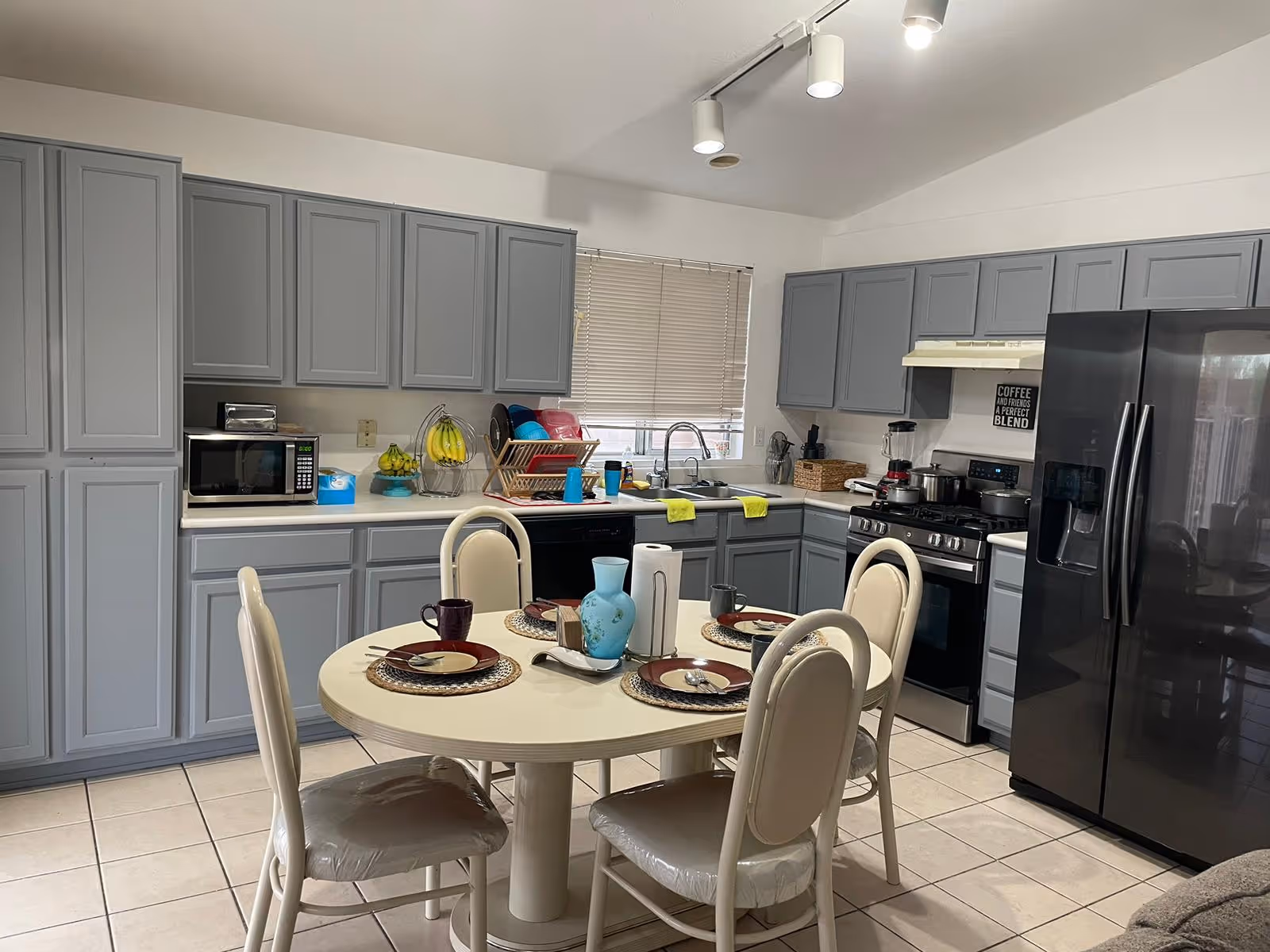 Bright kitchen with gray cabinets, a black refrigerator and a round dining table set for four in the center.