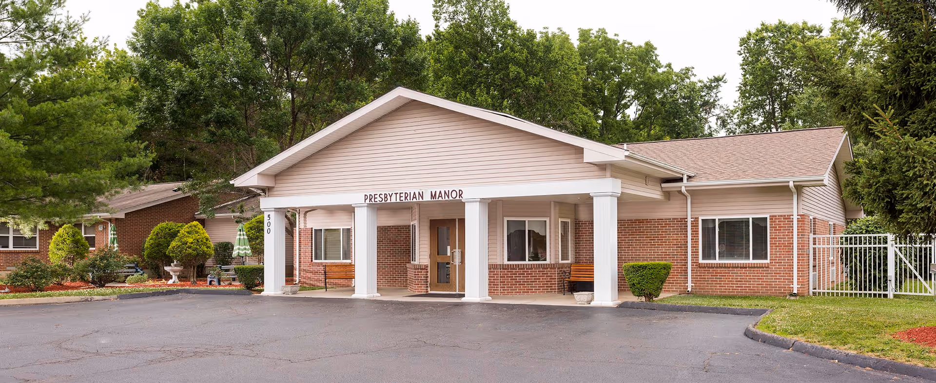 Front entrance of a single-story brick building with a covered portico and columns labeled 'Presbyterian Manor'.