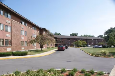 Brick senior housing building with a curved driveway and parked cars.