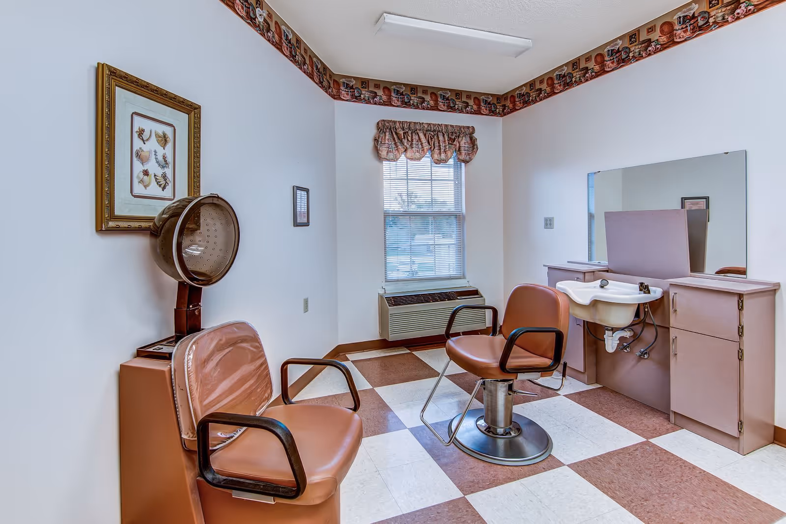 Small salon room with two styling chairs, a hooded hair dryer, a sink and mirror, and a checkered tile floor.