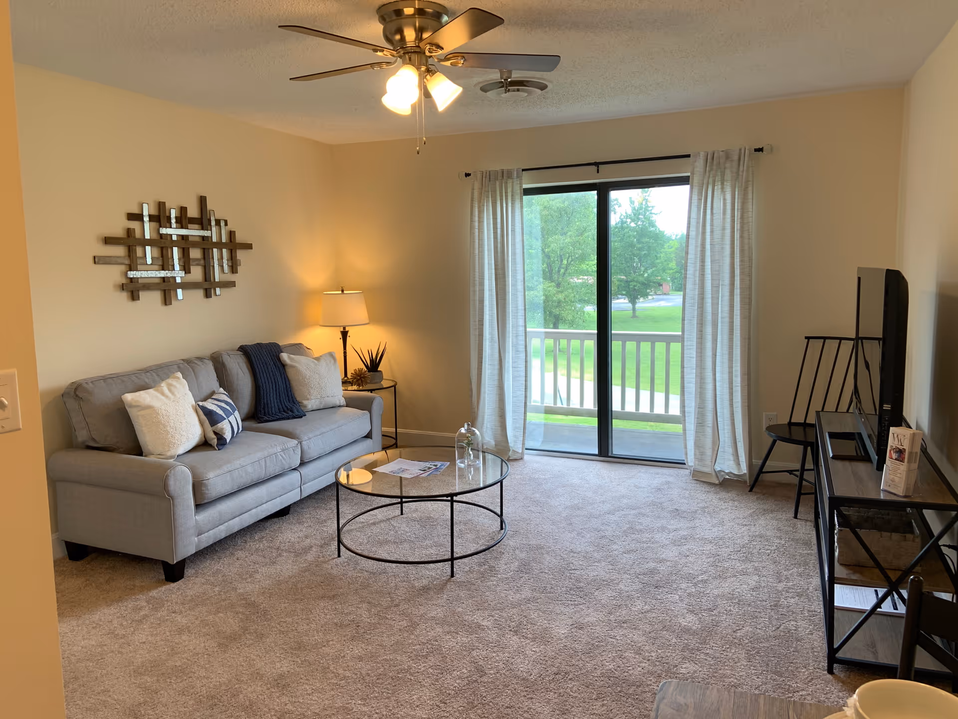 Bright living room with a gray sofa, round glass coffee table, TV console and sliding glass door opening to a balcony.