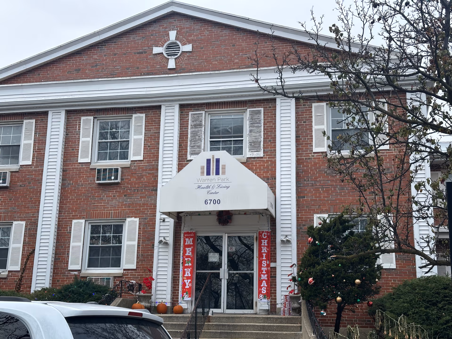 Brick facade and main entrance of Warren Park Health & Living Center with a white awning, steps, and holiday decorations.