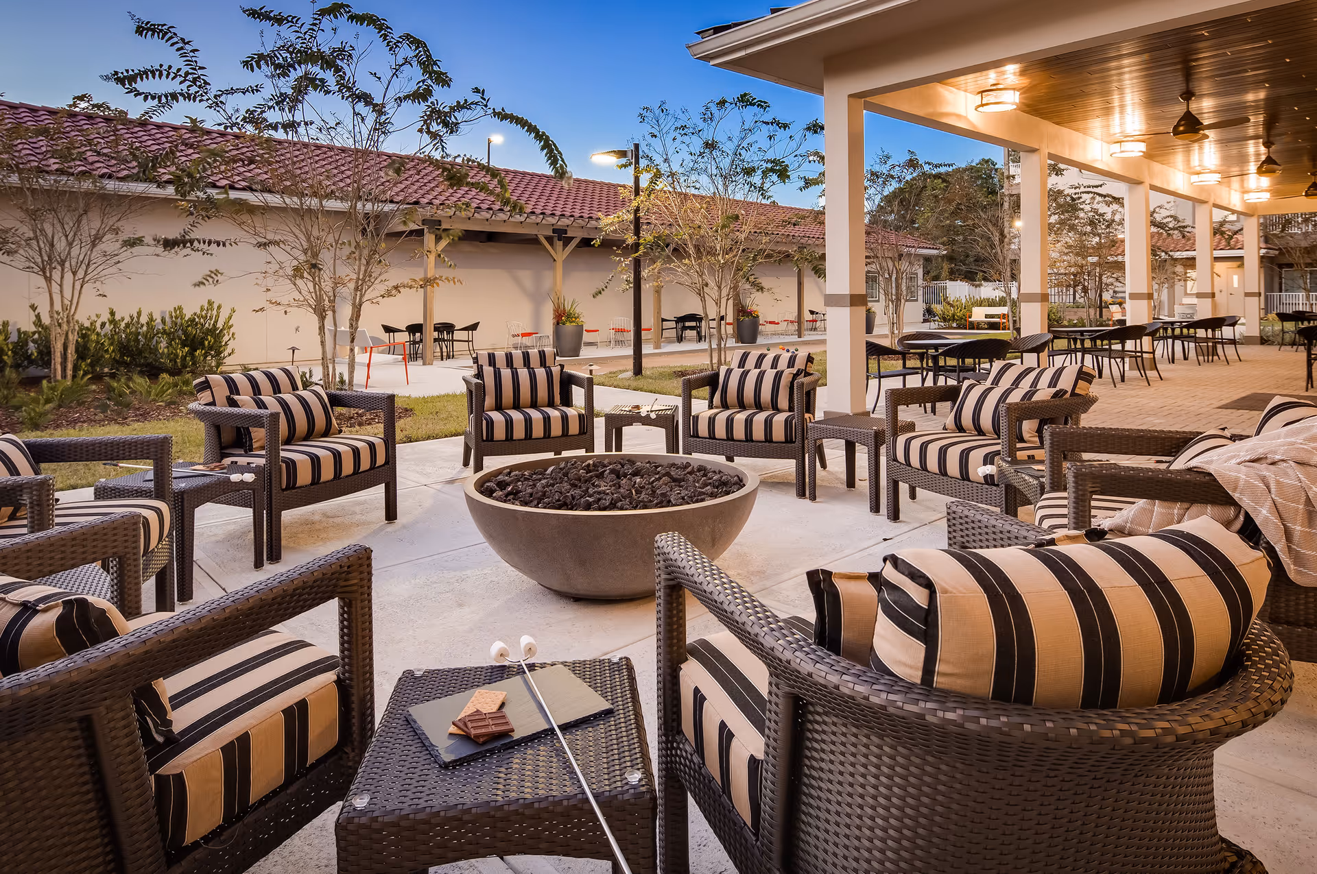 Outdoor patio with striped-cushioned wicker chairs arranged around a central fire pit under a covered pergola.