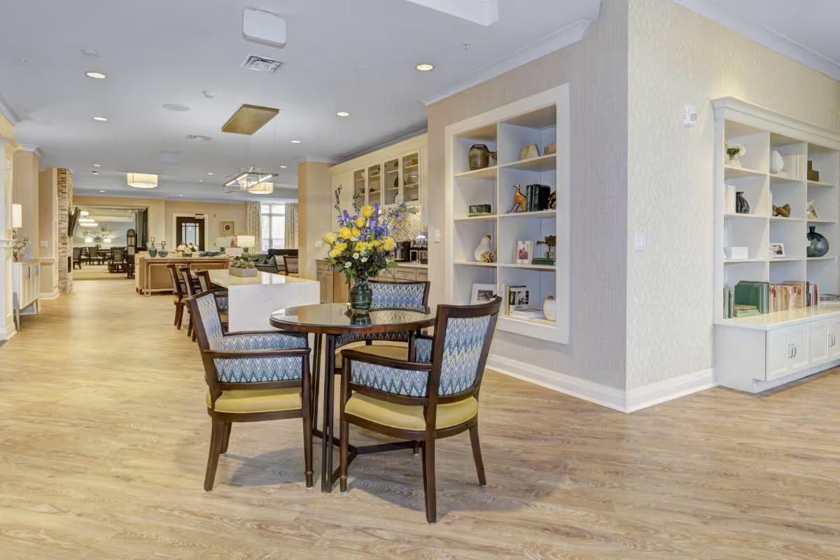 Bright communal seating area with a round table, upholstered chairs, built-in shelving and wood floors.