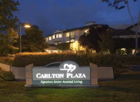 Nighttime exterior of Carlton Plaza Senior Living with illuminated front sign.