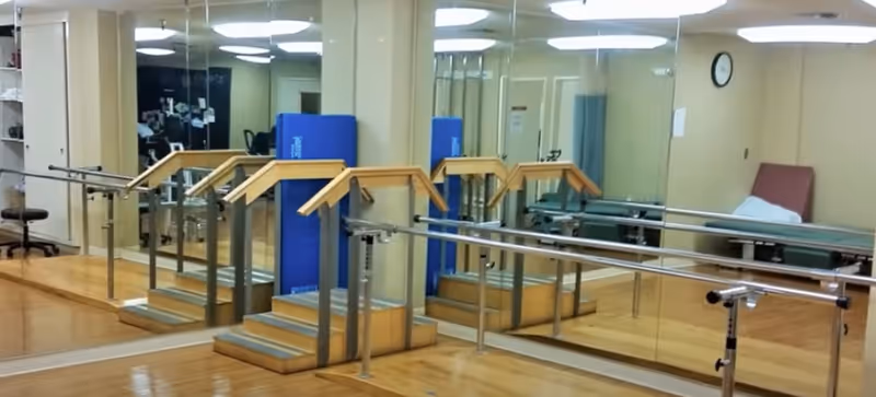 Rehabilitation/exercise room with parallel bars, a small practice staircase, wall mirrors and a treatment table.