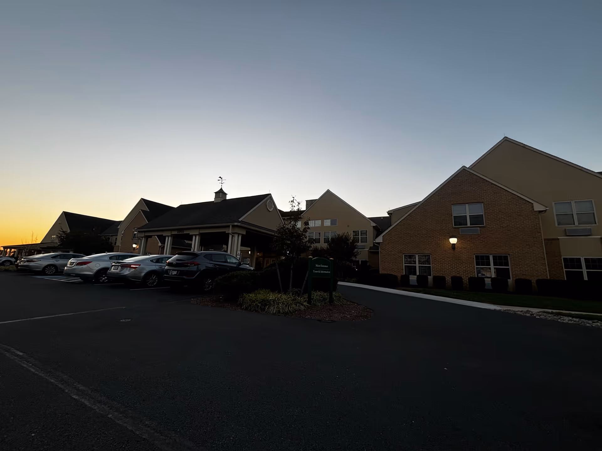 Front exterior of a retirement community building at dusk with cars parked in the driveway.