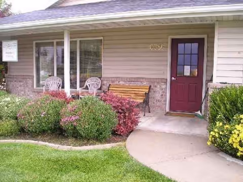 Front entrance of Brighton House Assisted Living with benches, chairs, and landscaped shrubs.