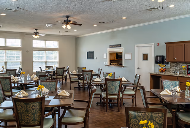 Bright dining room with multiple set tables and chairs, ceiling fans, and a serving counter/window.