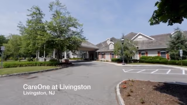 Exterior view of CareOne at Livingston facility showing a driveway leading to the entrance of a single-story building surrounded by trees and landscaping under a clear sky.