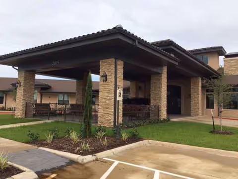 Stone pillar entrance canopy at Clayton Oaks Living with landscaping and parking area.