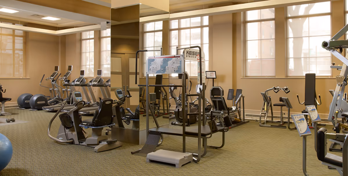 Well-lit fitness room with cardio machines, weight equipment, and large windows.
