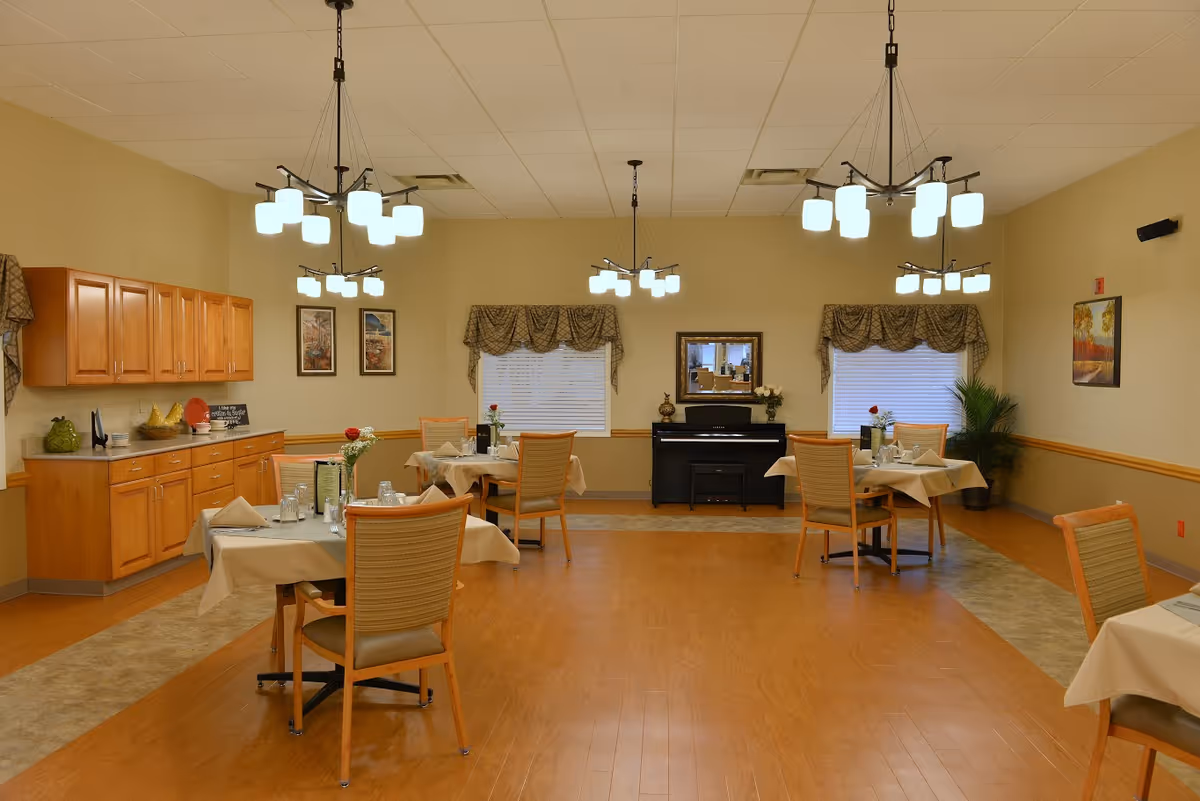 Cozy dining room with set tables and chairs, pendant lights, cabinets along the left wall, and a piano against the back wall.