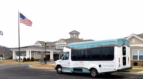 Exterior view of a senior living building with a parked shuttle bus in front.