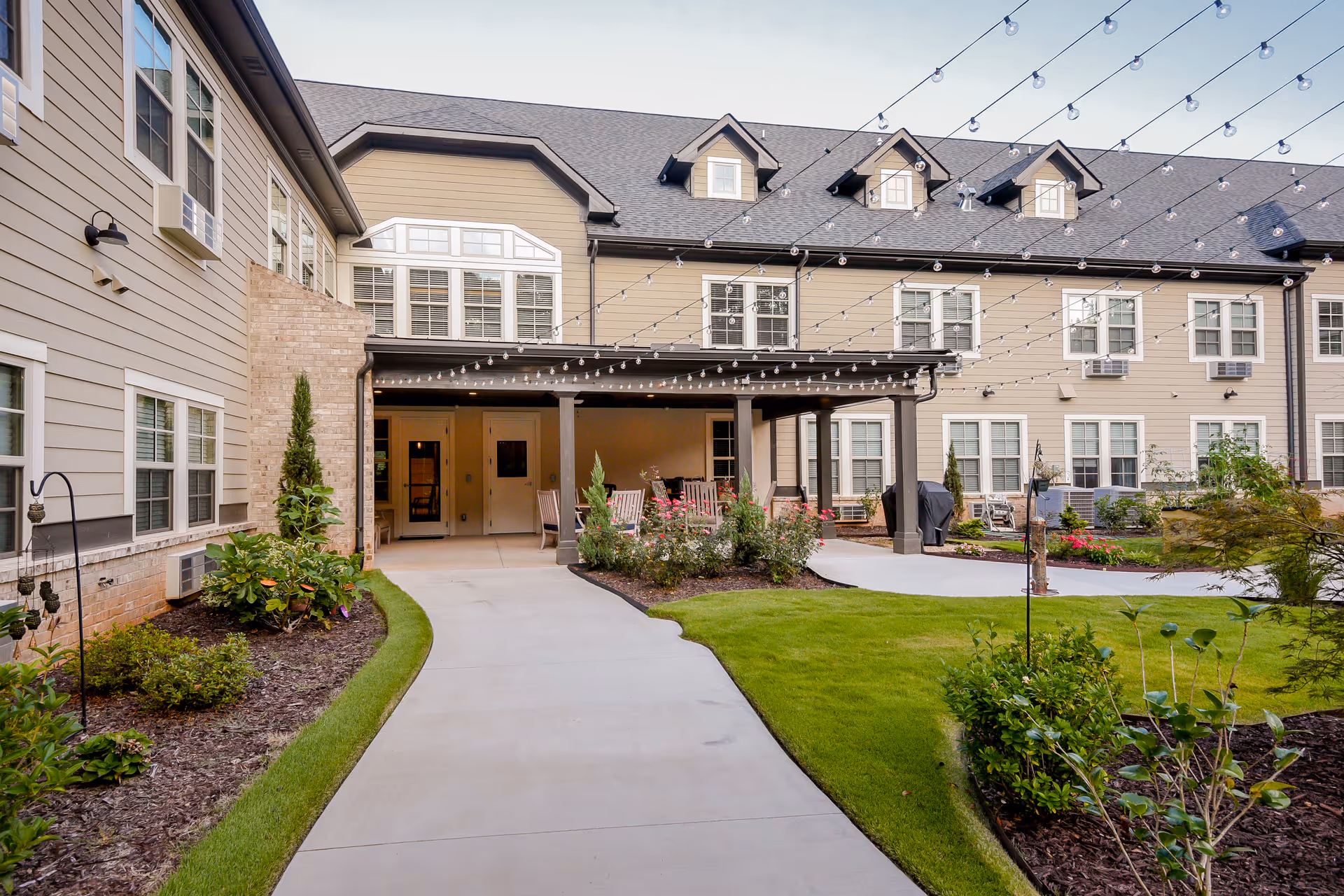 Courtyard view of Orchard at Brookhaven's exterior showing a covered patio with string lights, a walkway, and landscaped gardens.