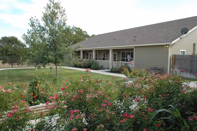 Single-story building with a covered front porch, walkway, lawn and flowering shrubs in the foreground.