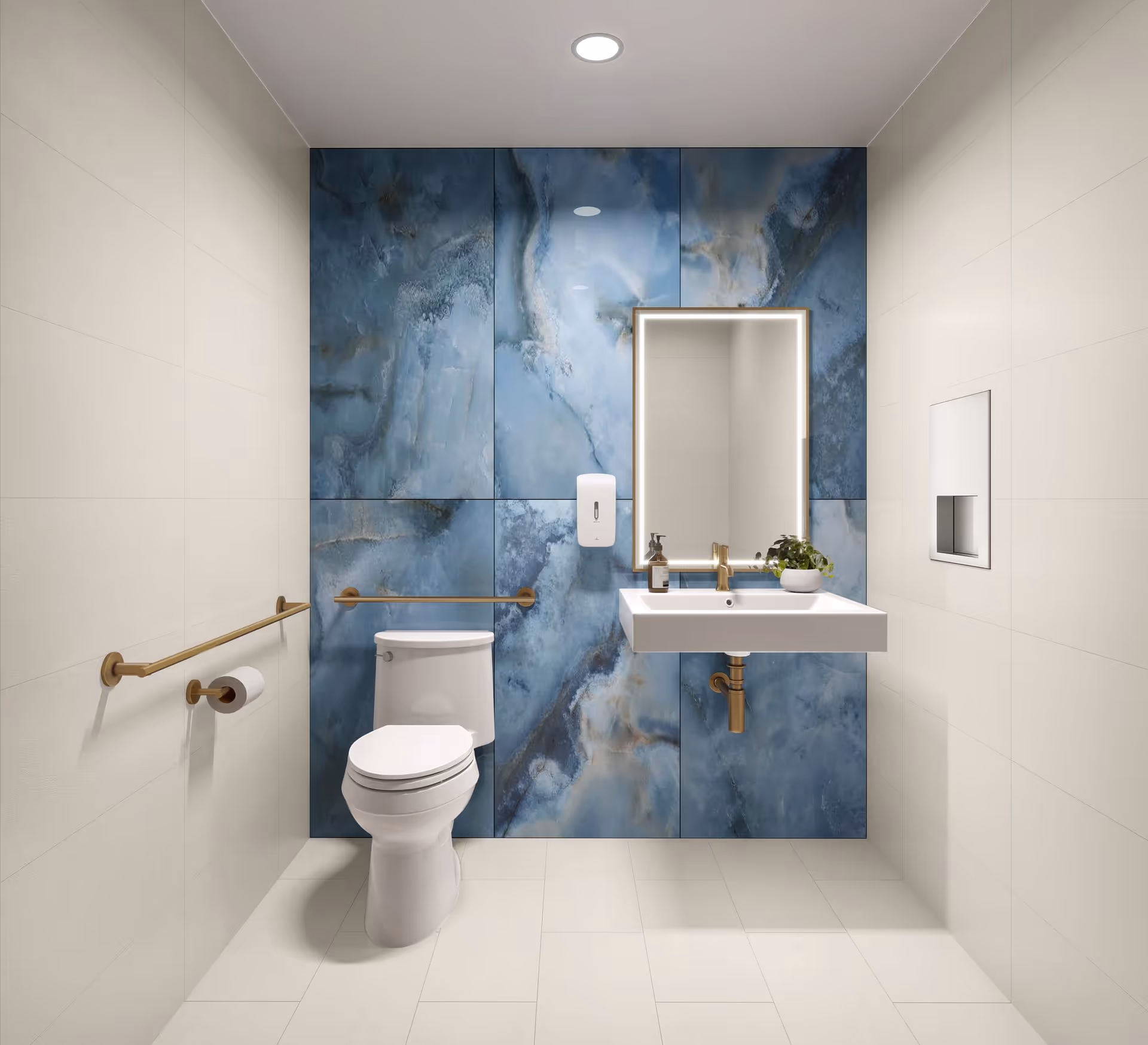 A modern bathroom with white tiled walls and floor, featuring a white toilet and a wall-mounted white sink with gold fixtures. The back wall has large blue marble-patterned tiles. Above the sink is a rectangular mirror with built-in lighting. There are gold handrails on the walls and a soap dispenser mounted next to the mirror.