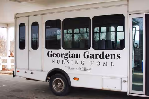 White bus with Georgian Gardens Nursing Home sign parked beside facility exterior.