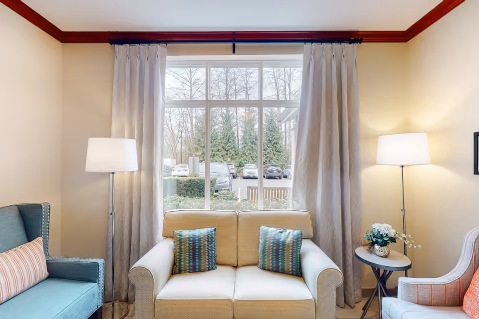 Cozy seating area with a loveseat and armchairs in front of a large window, flanked by floor lamps and a side table with flowers.