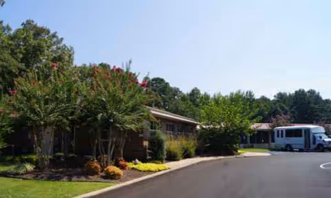 Exterior view of Tupelo Nursing & Rehab Center with landscaped shrubs and a parked shuttle bus.
