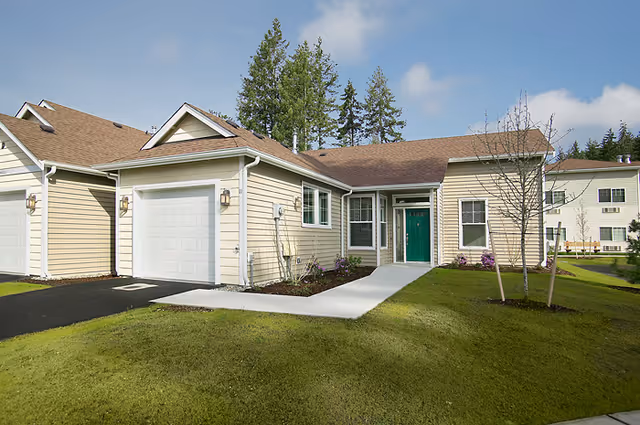 Front exterior of a beige single-story residential unit with an attached garage, green front door, and a manicured lawn under a blue sky.