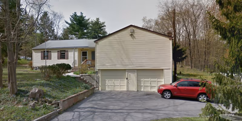 Exterior view of a residential-style care facility with driveway and red car.