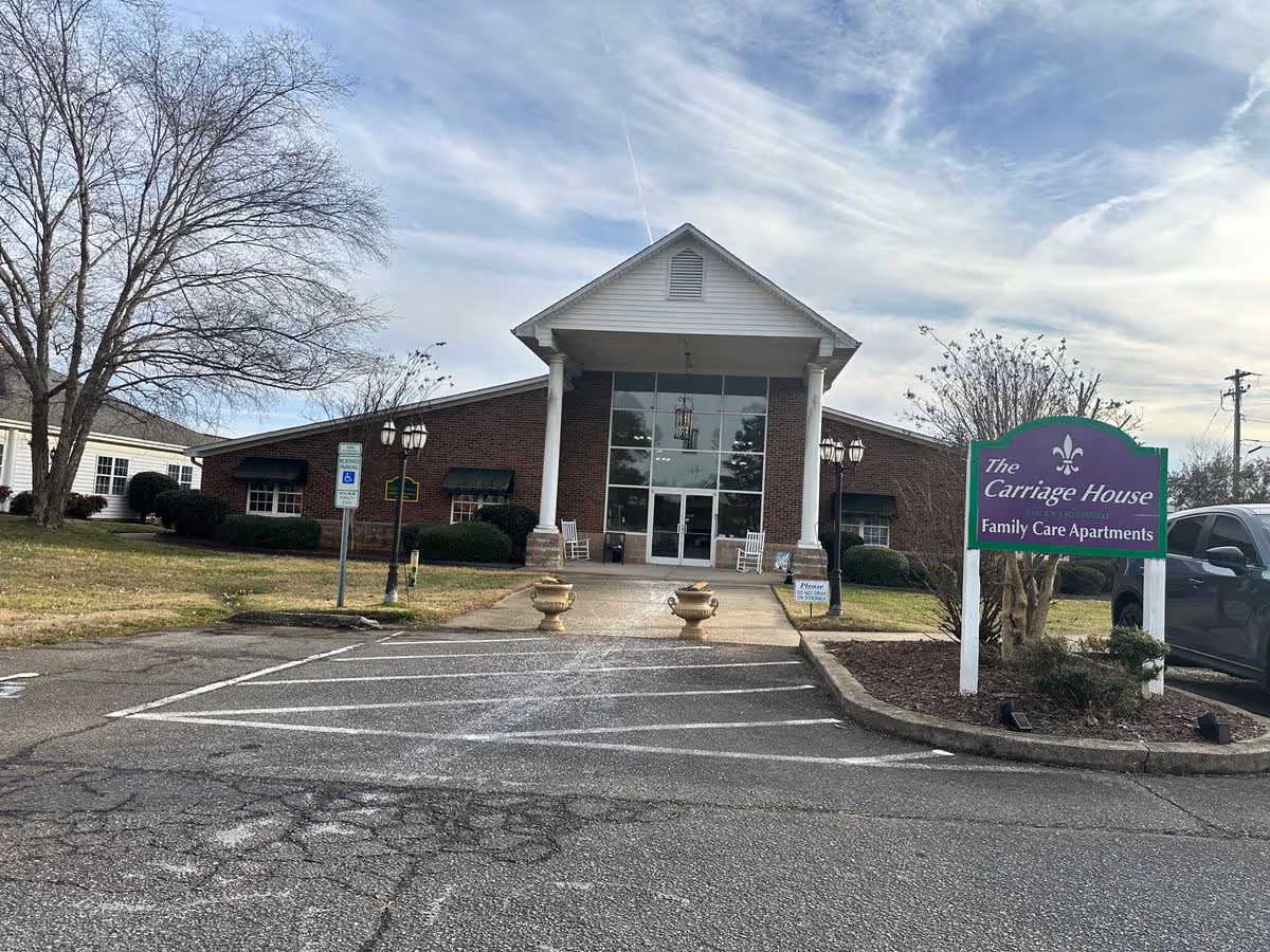 Front entrance of a brick retirement facility with columns, glass doors, a driveway and a sign reading "The Carriage House Family Care Apartments."