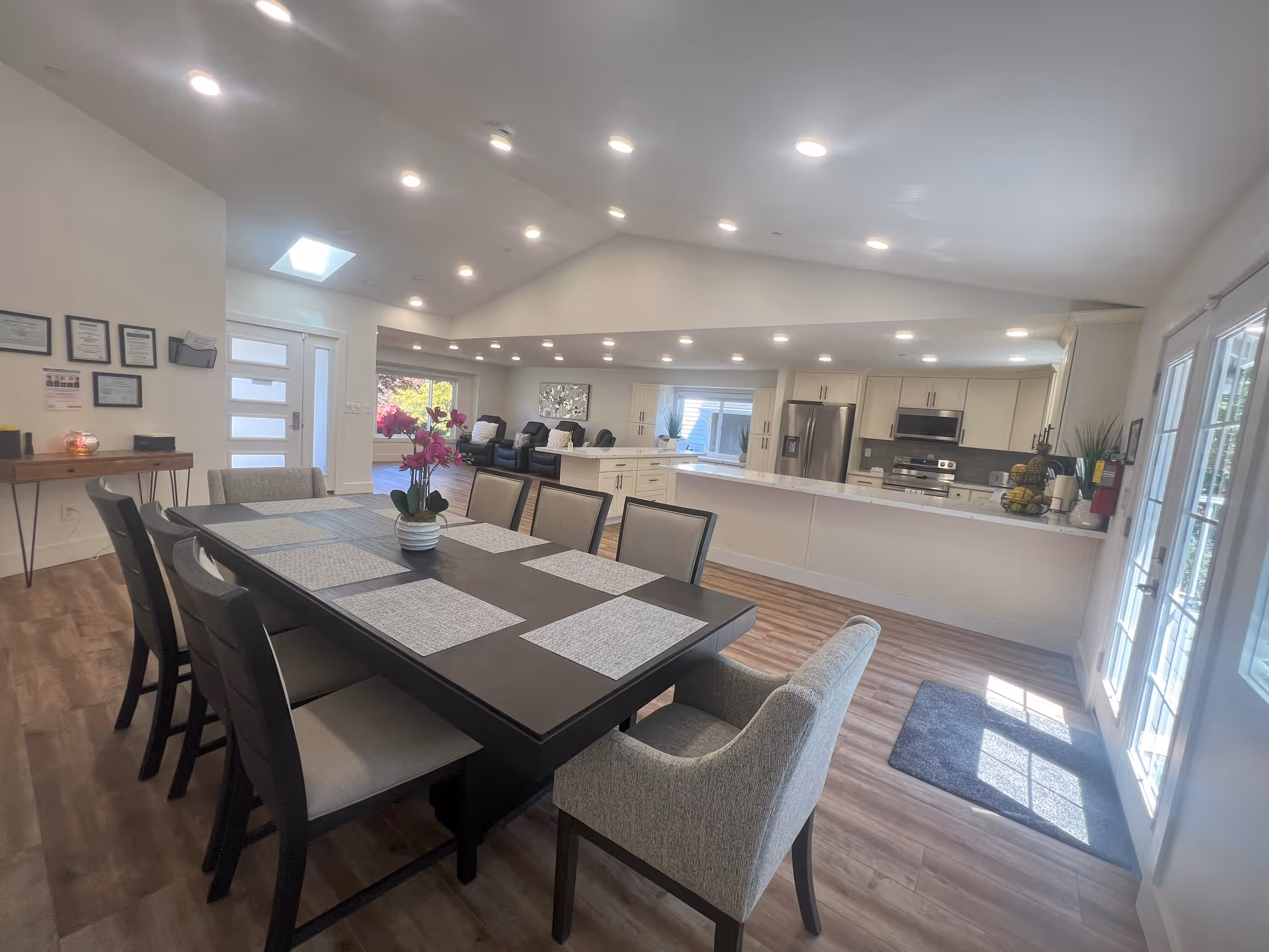 Bright open dining area with a large table and chairs facing a modern open kitchen and living space.
