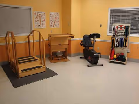 A small exercise room with a stationary bike, wooden ramp, and fitness equipment.