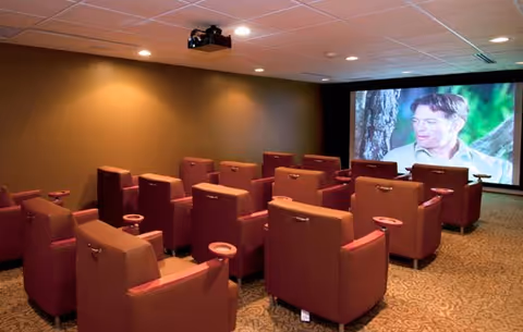 Small screening room with rows of upholstered recliners facing a large projection screen playing a movie.