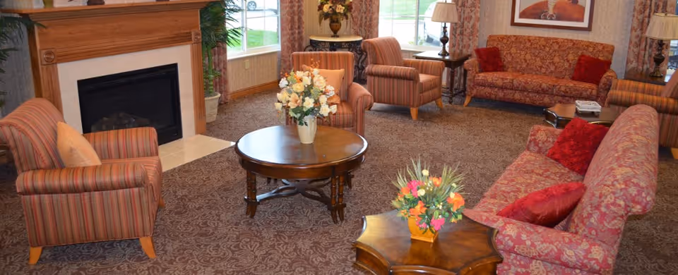 Communal living room with patterned sofas and armchairs arranged around coffee tables and a fireplace.