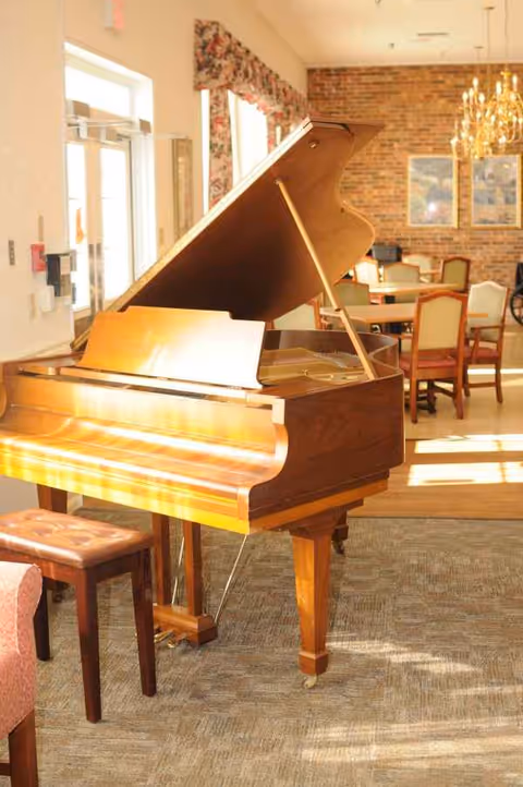 Wooden grand piano in a sunlit senior living common room.