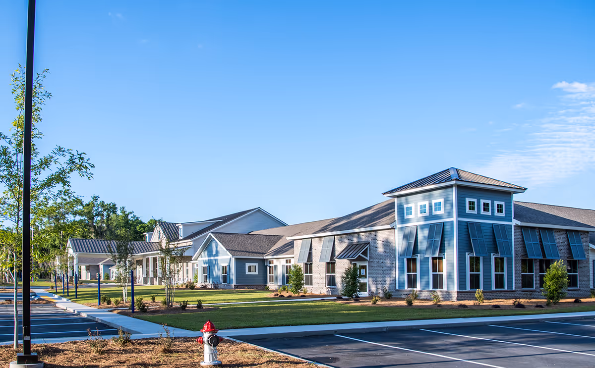 Exterior view of Sprenger Health Care of Port Royal building with blue sky, landscaped lawn, trees, and an empty parking lot with a fire hydrant in the foreground.