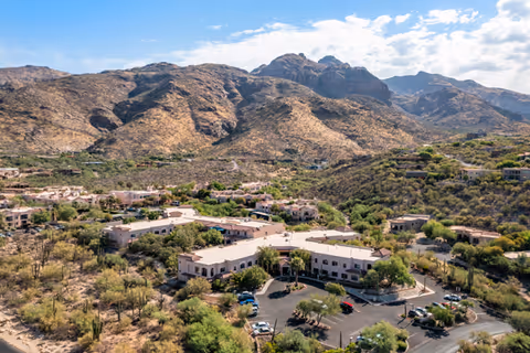 Aerial view of Brookdale Santa Catalina senior living facility surrounded by desert landscape and mountains under a partly cloudy sky.