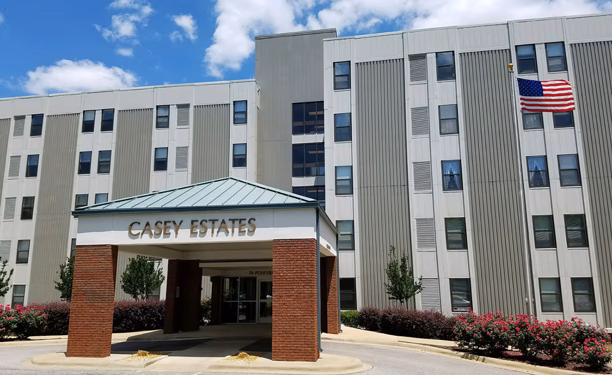 Front entrance of a multi-story building labeled Casey Estates with a covered porte-cochère and an American flag.