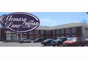 Exterior view of a two-story brick building with multiple windows and a parking lot in front containing several parked cars. A sign on the building reads 'Memory Lane and Rehab Valley View'.