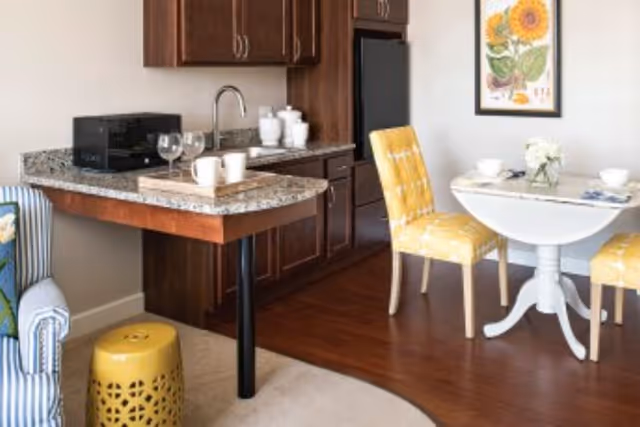 Small kitchenette and dining area with a granite countertop, yellow upholstered chairs, and a round white table.