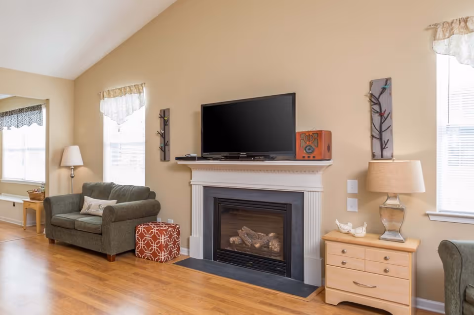 Bright living room featuring a fireplace with a television on the mantel, a green loveseat, side tables and lamps.
