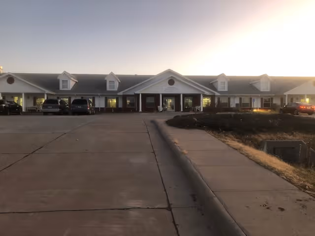 Front exterior of a single-story assisted living building with a parking lot and main entrance at dusk.