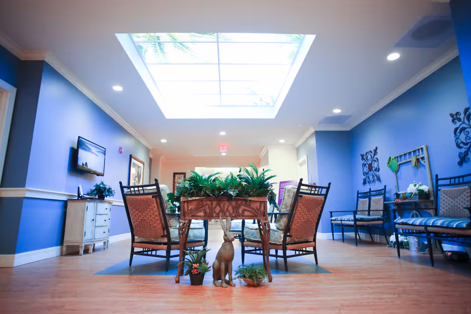 Bright communal lounge with chairs around a central planter under a large skylight and blue walls.