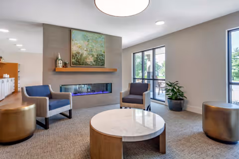 Modern lounge with armchairs, a round coffee table, a fireplace and large windows.