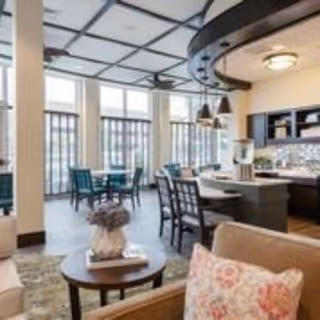 Bright communal dining and lounge area with tables, chairs, a kitchen island, and large windows.