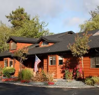 Red wooden senior living lodge front with American flag, plants, and trees.