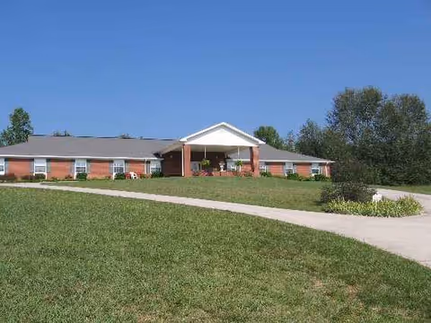 Single-story brick senior living facility with a front entrance, lawn, and blue sky.