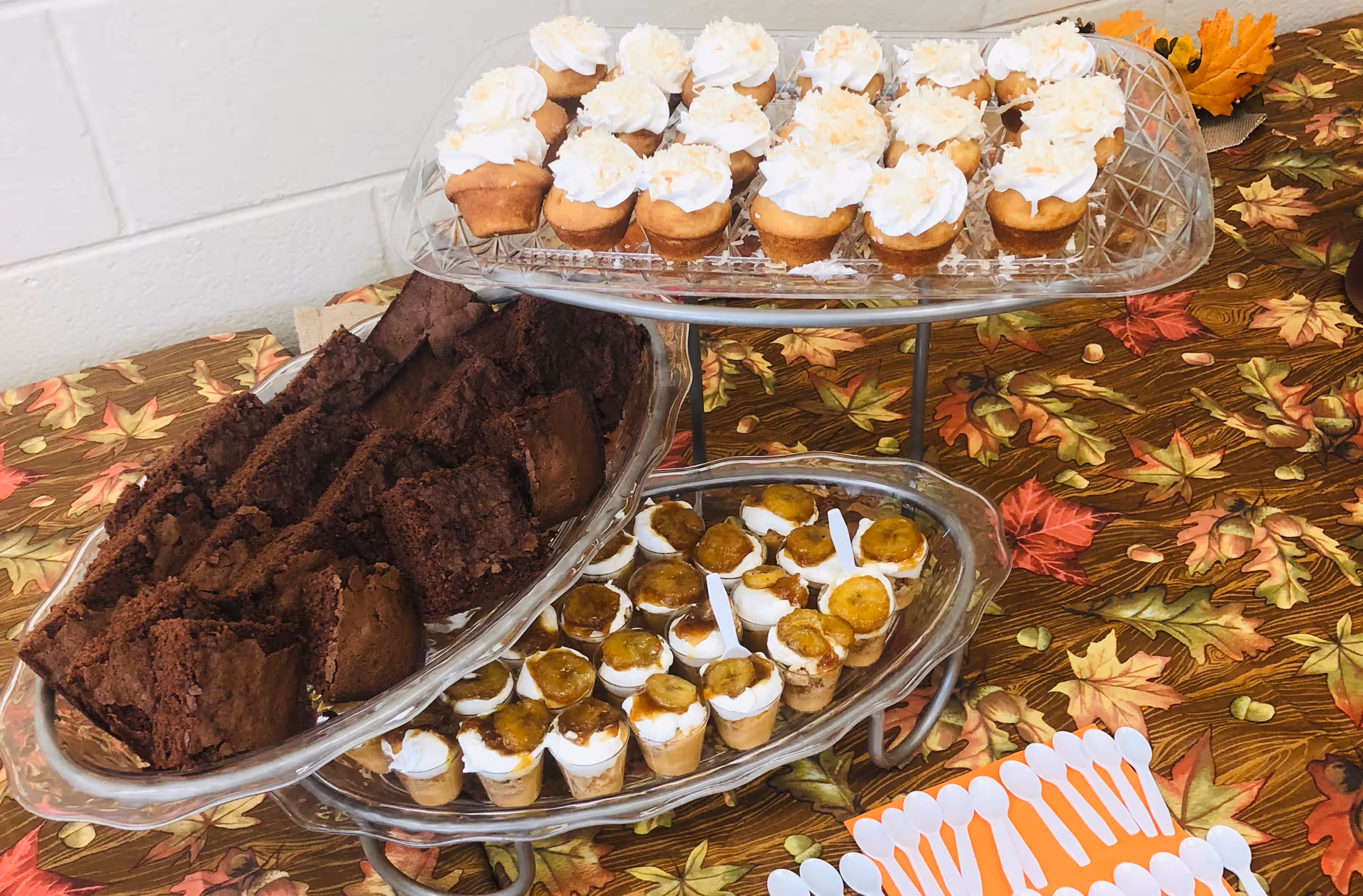 Tiered dessert display with cupcakes, brownies, and bite-sized treats on an autumn-themed tablecloth.