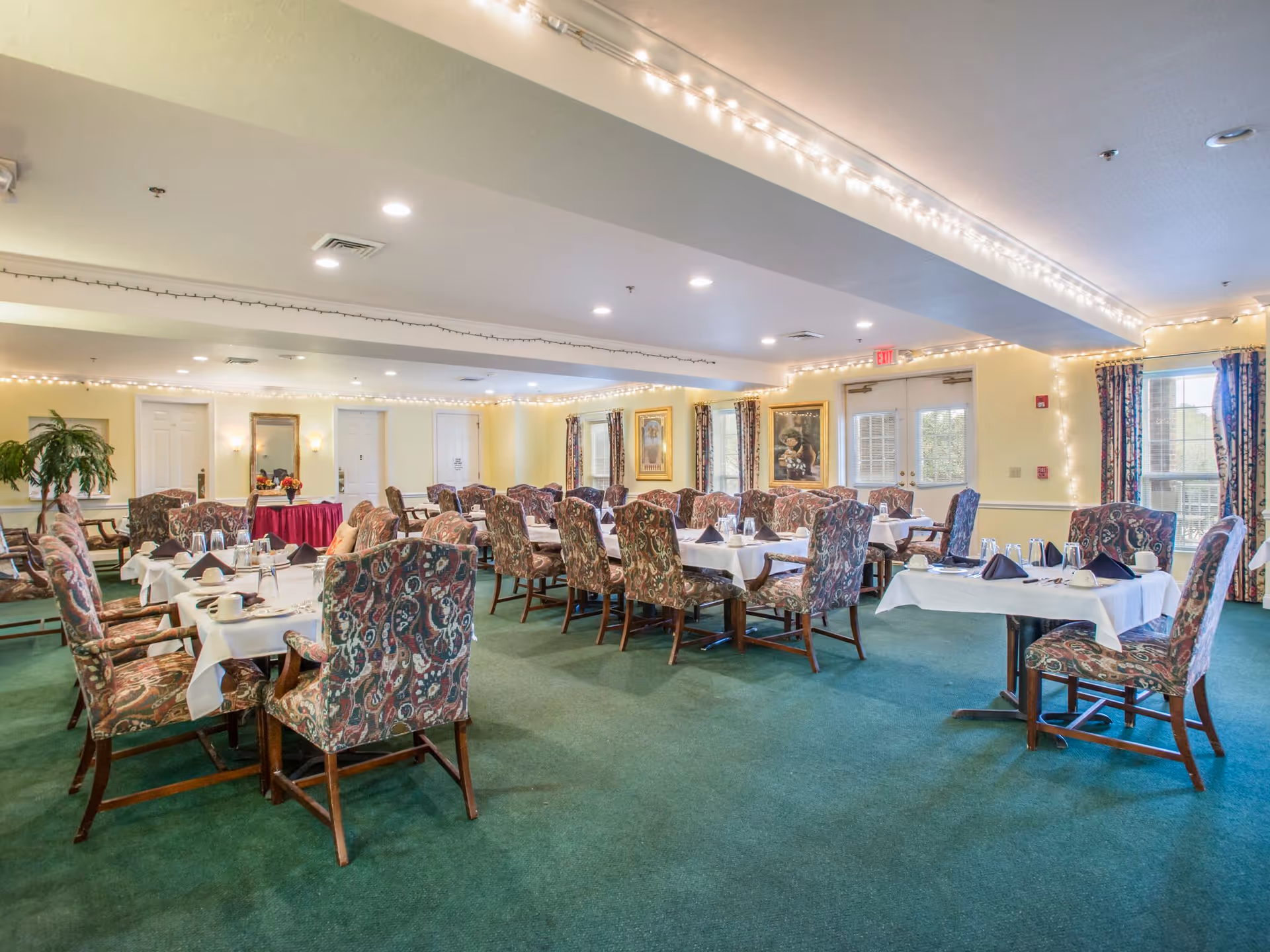 Spacious dining room with multiple tables set with white tablecloths and patterned upholstered chairs.